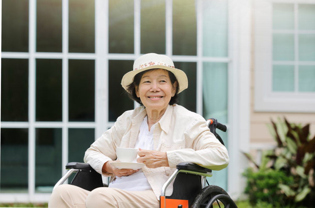 An asian elderly woman on a wheelchair is smiling happily while looking at something in front of her.