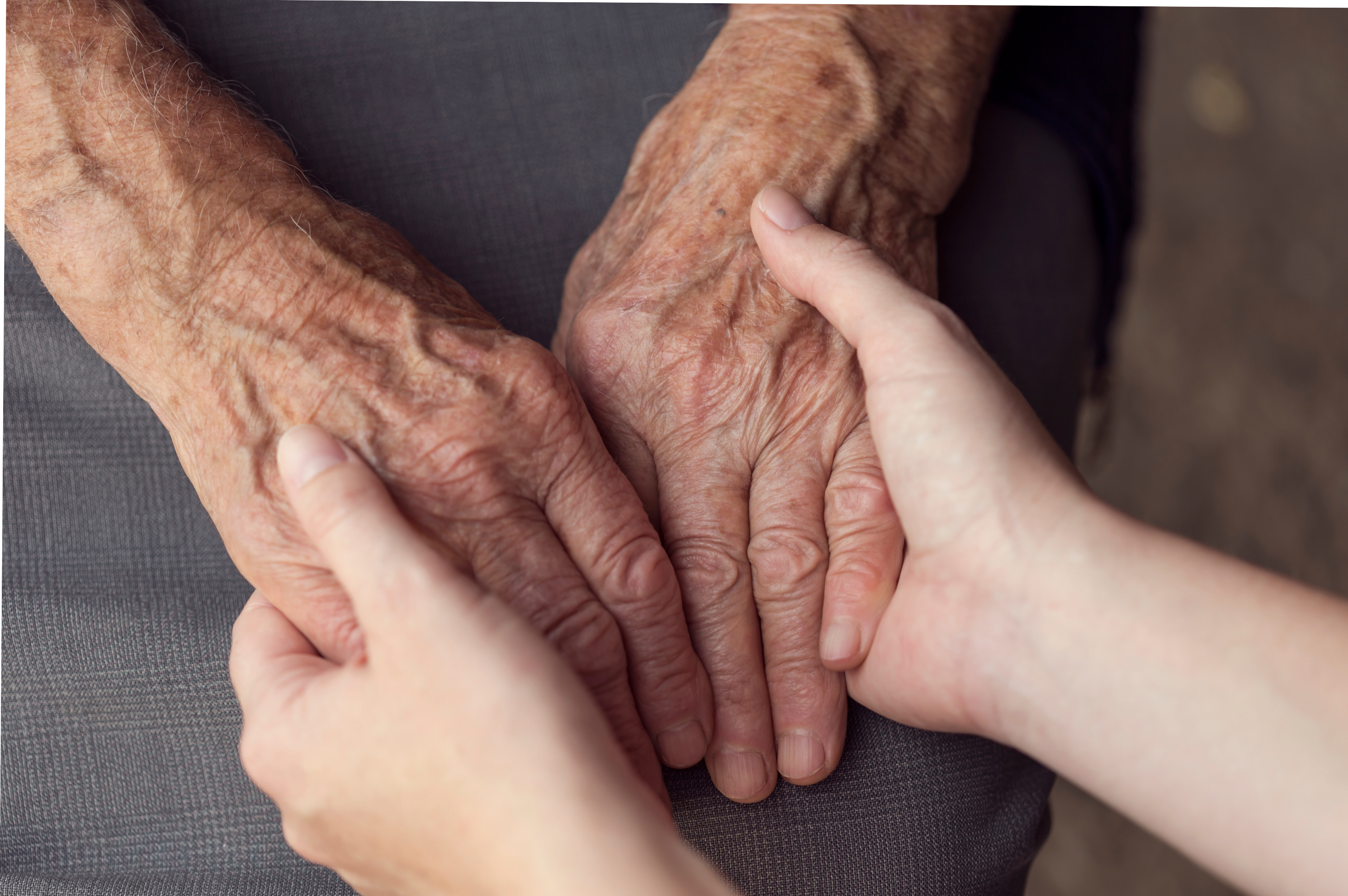 Close up of young hands holding both hands of an elderly person.